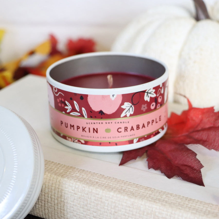 Scented candle in a decorative tin with 'Pumpkin Crabapple' label on a surface with autumn-themed decor.