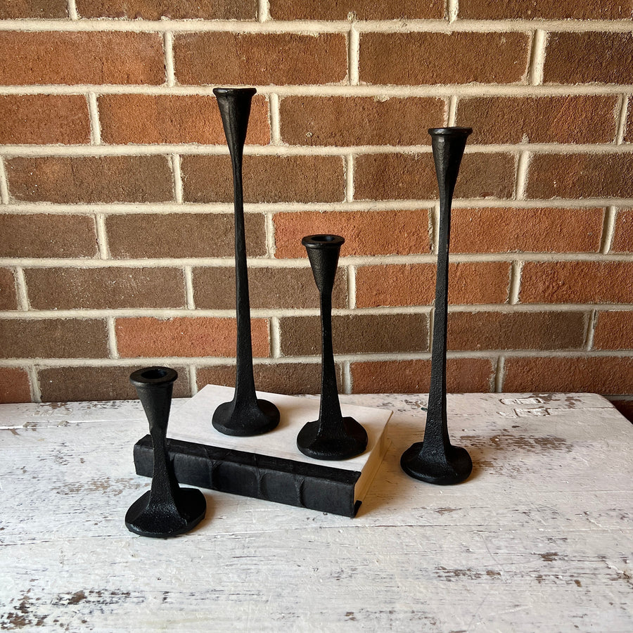 Set of black candlesticks on a white surface with a brick wall background